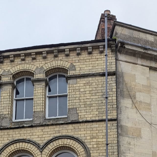 Gutter vacuum pole reaching the roofline of a tall stone building in Cirencester